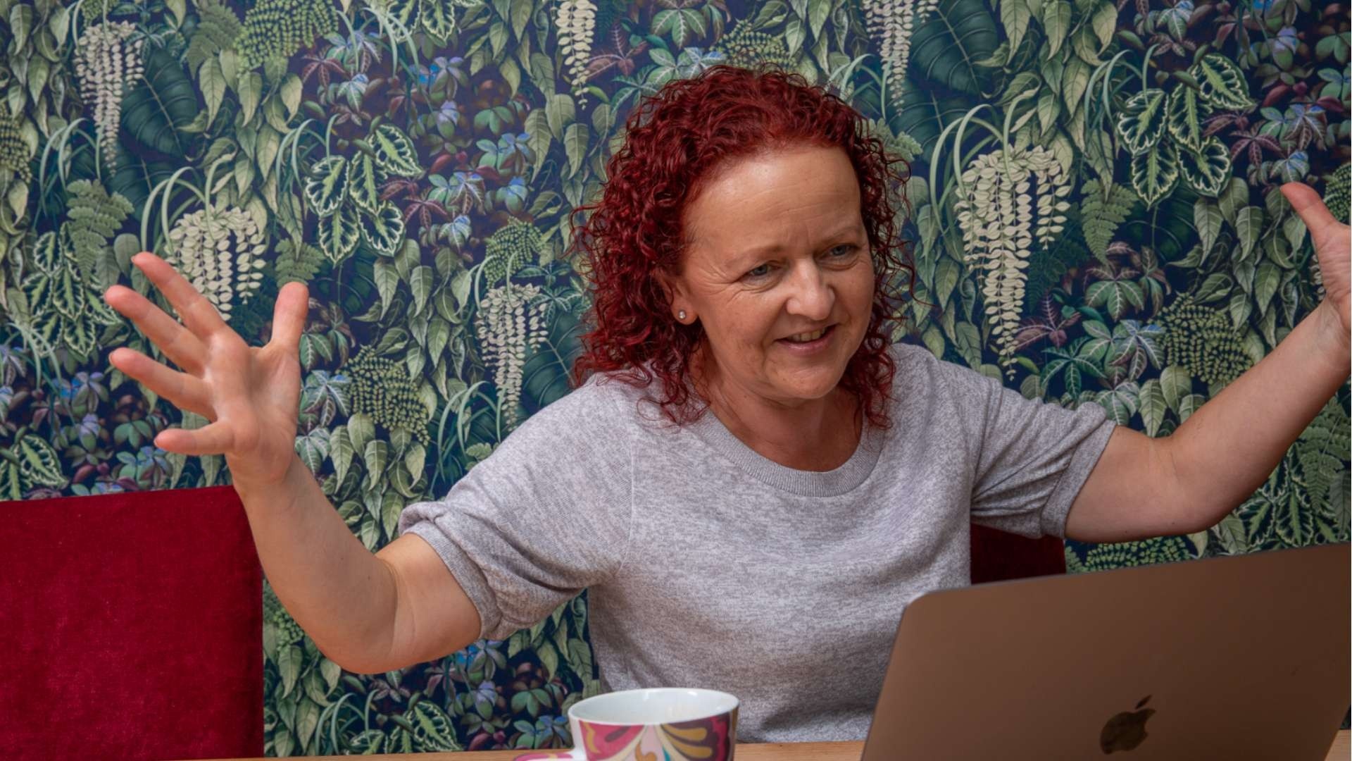 Photo portrait of Claire Waite Brown of Creativity Found, talking and gesturing with her arms in front of a computer