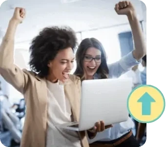 two women in an office with fist raised in celebration looking at laptop screen