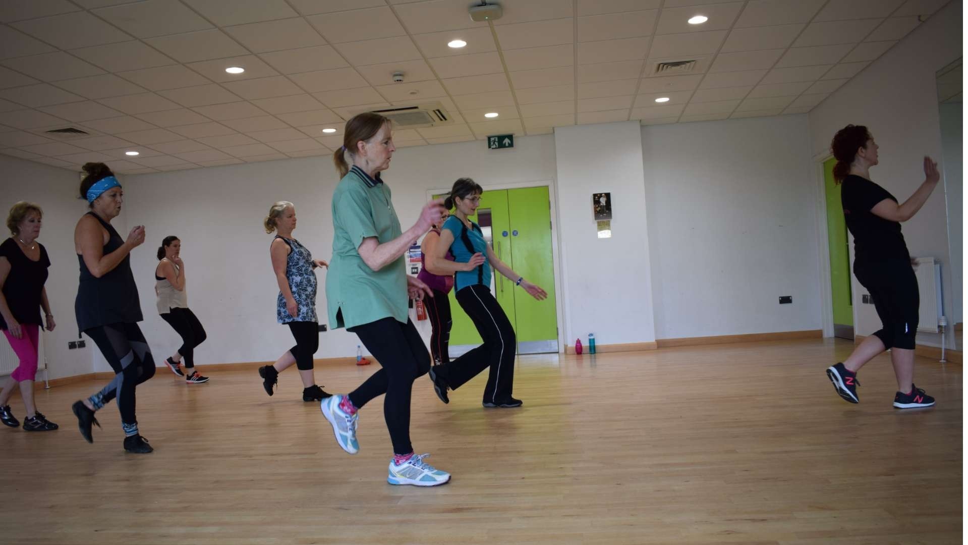 A dance class in action with the teacher on the far right and a group of women behind her following her movements