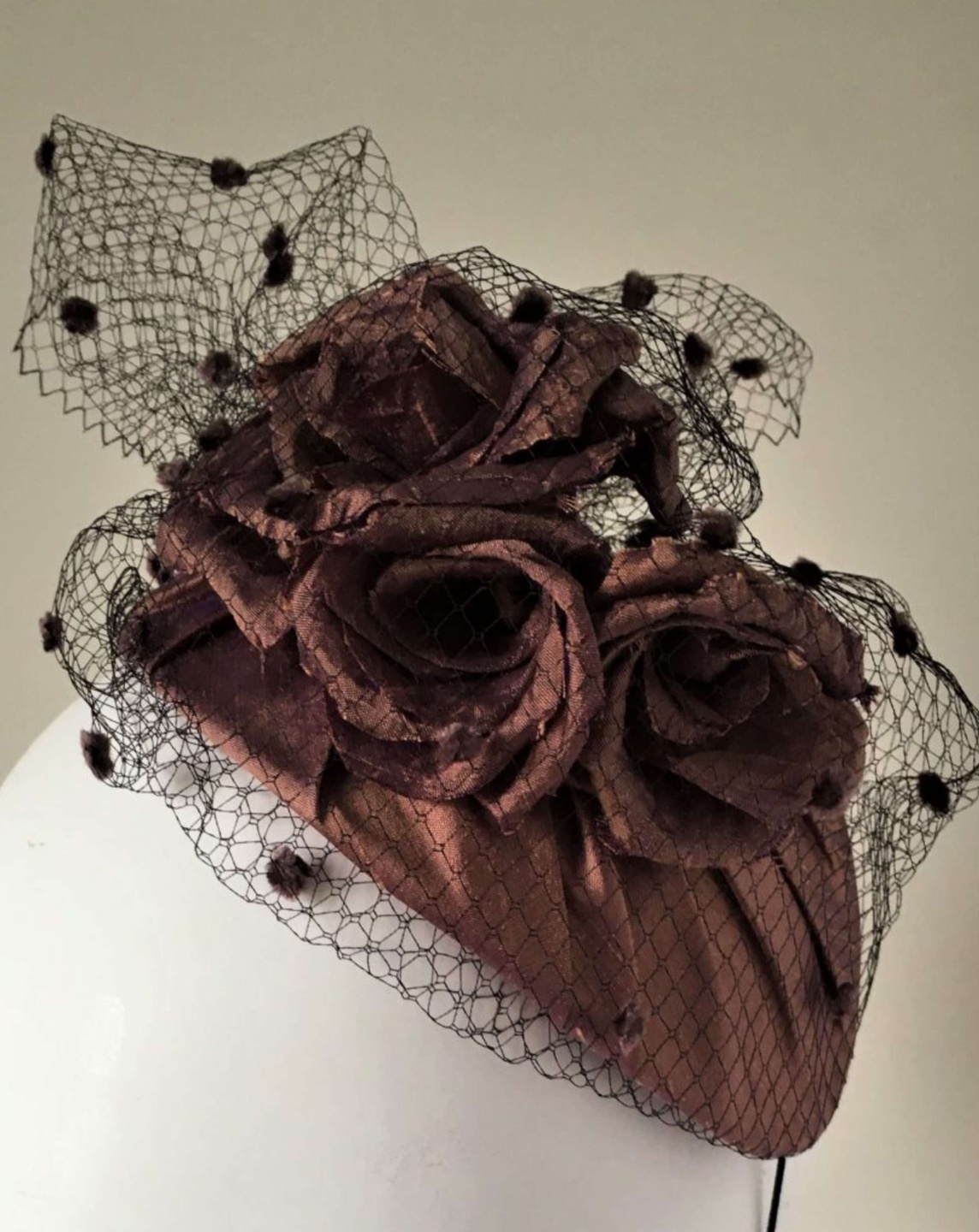 A brown fascinator with three roses surrounded by mesh, on a mannequin