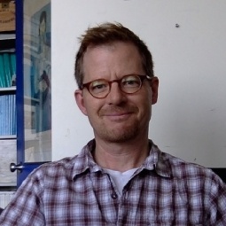 Photo of Dr. Robert Bruce Thompson, Professor of Psychology. Dr. Thompson is wearing a plaid shirt and books can be seen in the background.