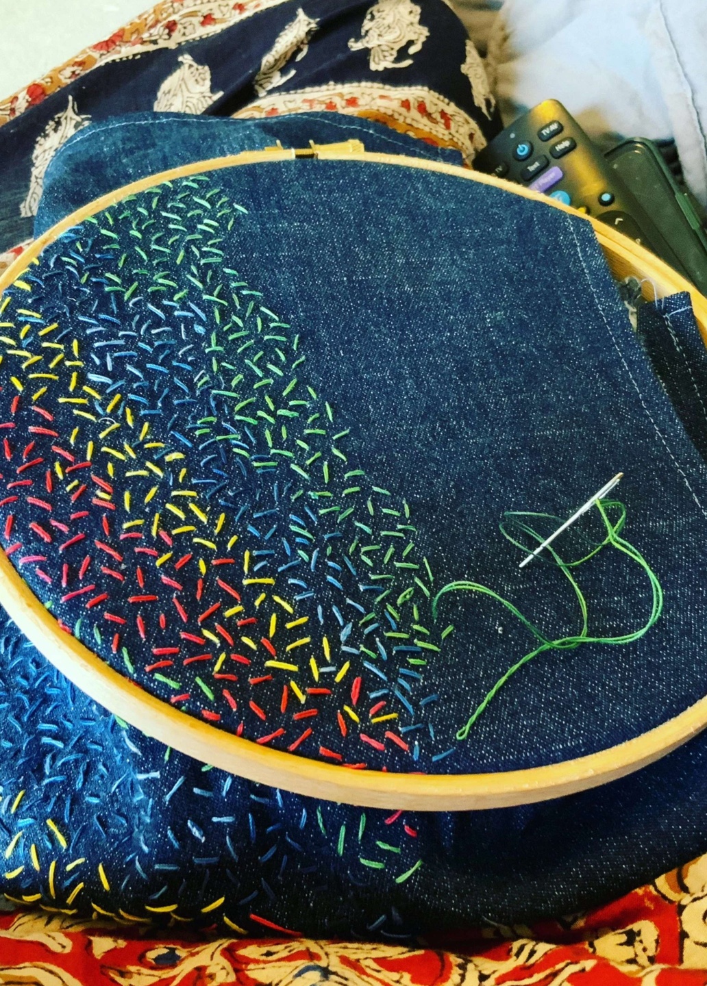 A denim style fabric in an embroidery hoop is half finished with abstract multicoloured stitches which look like hundreds and thousands