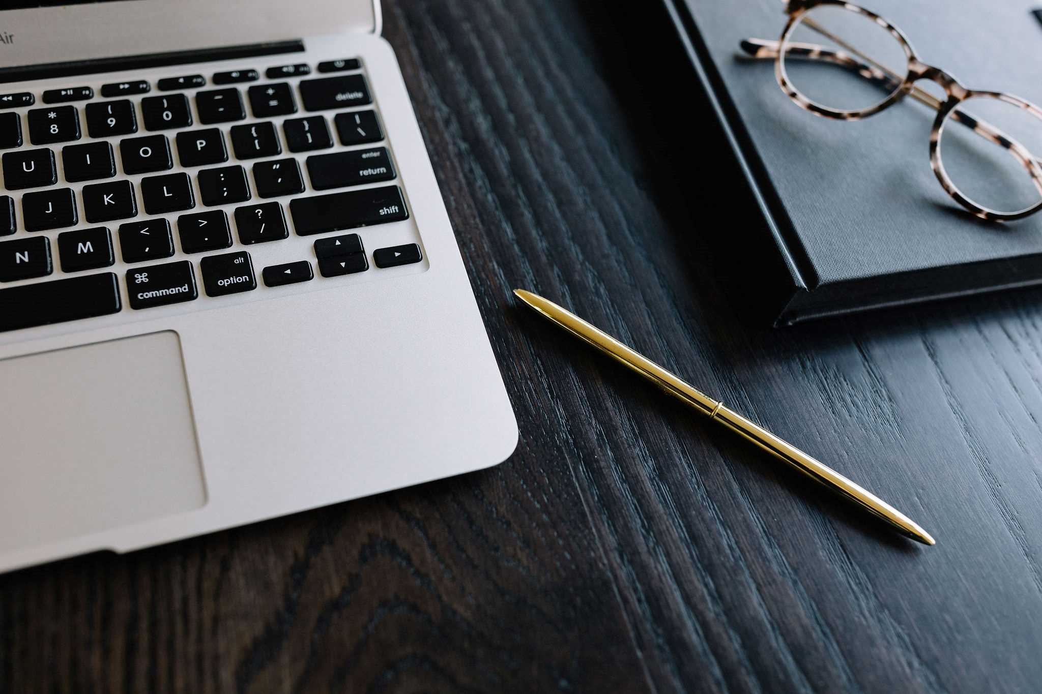 Flat lay of laptop gold pen and folded glasses on top of notebook