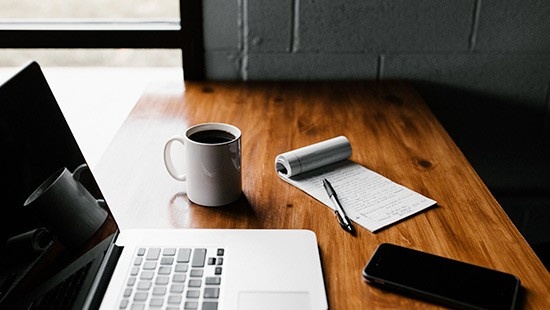 Coffee cup, laptop and notepad on desk