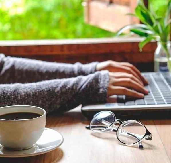 hands on keyboard, glasses and coffee cup on table