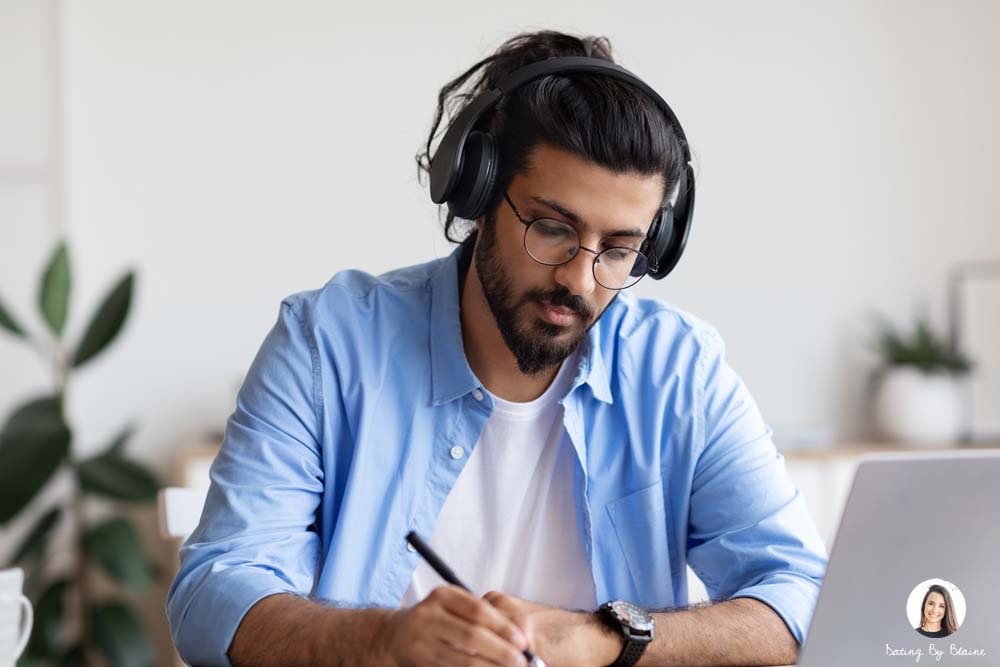 man with a headphone, writing in front of a laptop