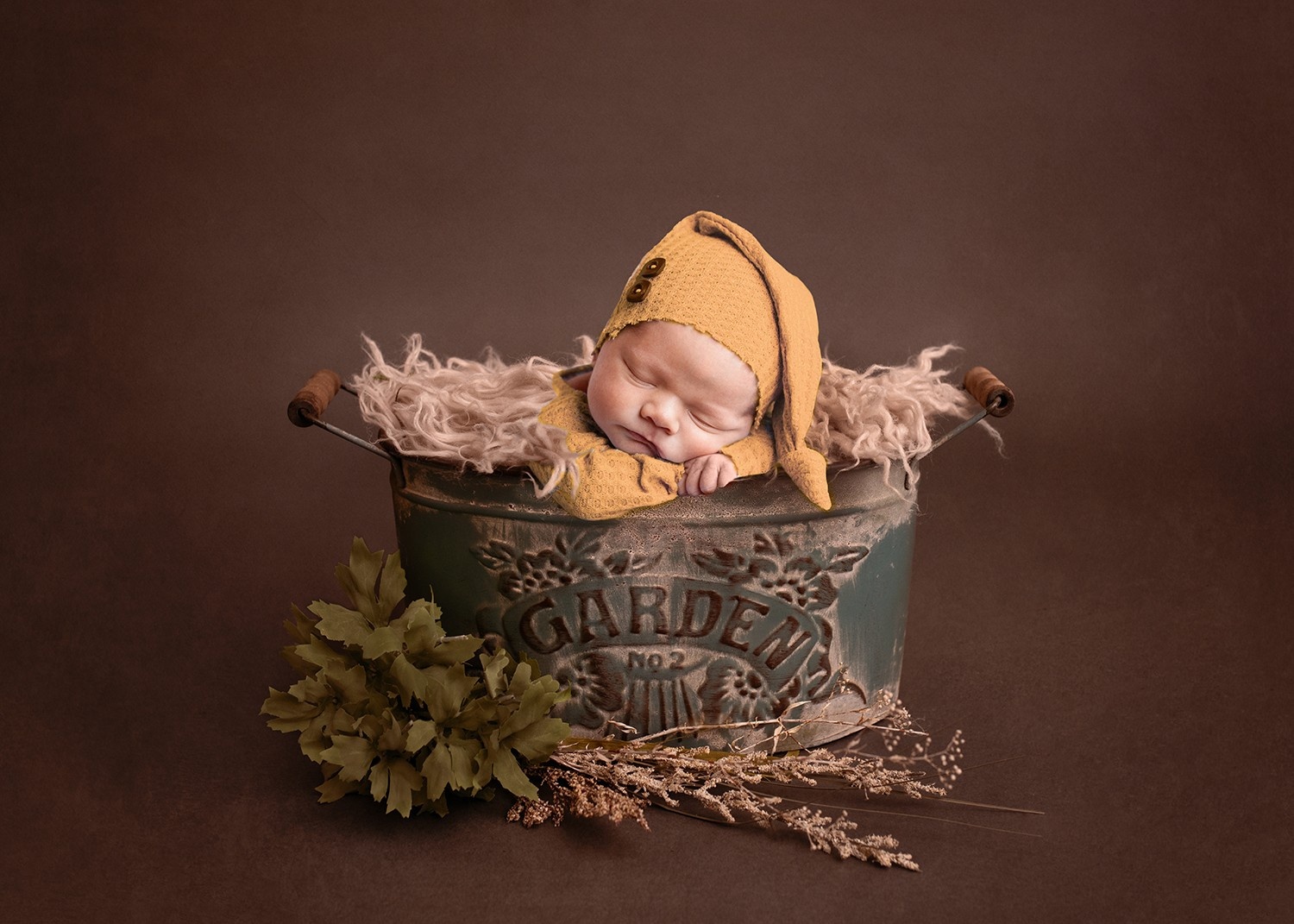 newborn dressed in gold with sleepy cap sleeping in garden bucket fall tones copyright rebecca peterman