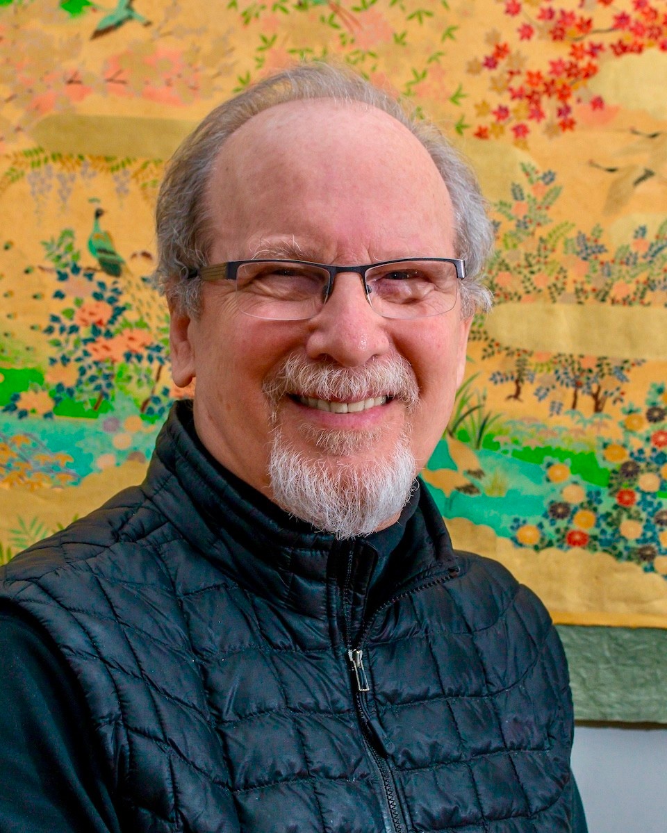 David Zemach-Bersin smiling in front of a colorful tapestry