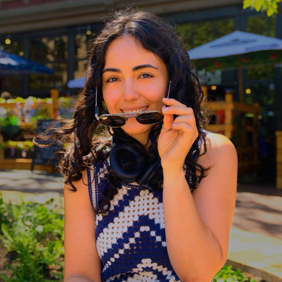 Yasi, your instructor, smiling outdoors with headphones around her neck