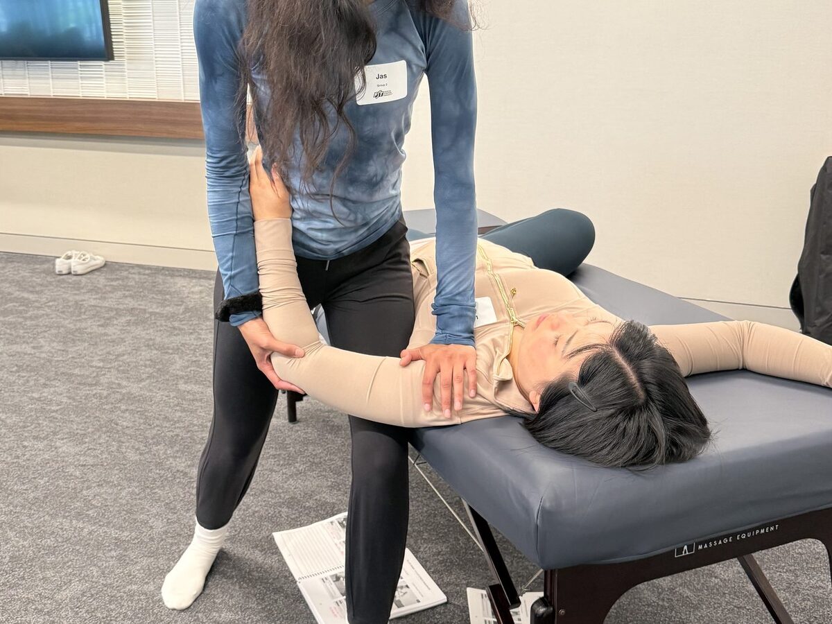 A student taking a clothed client's arm and shoulder through a stretch at the table