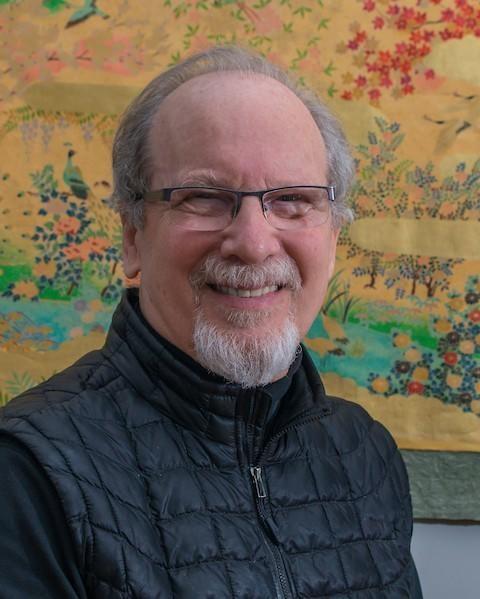 David Zemach-Bersin smiling in front of a colorful tapestry