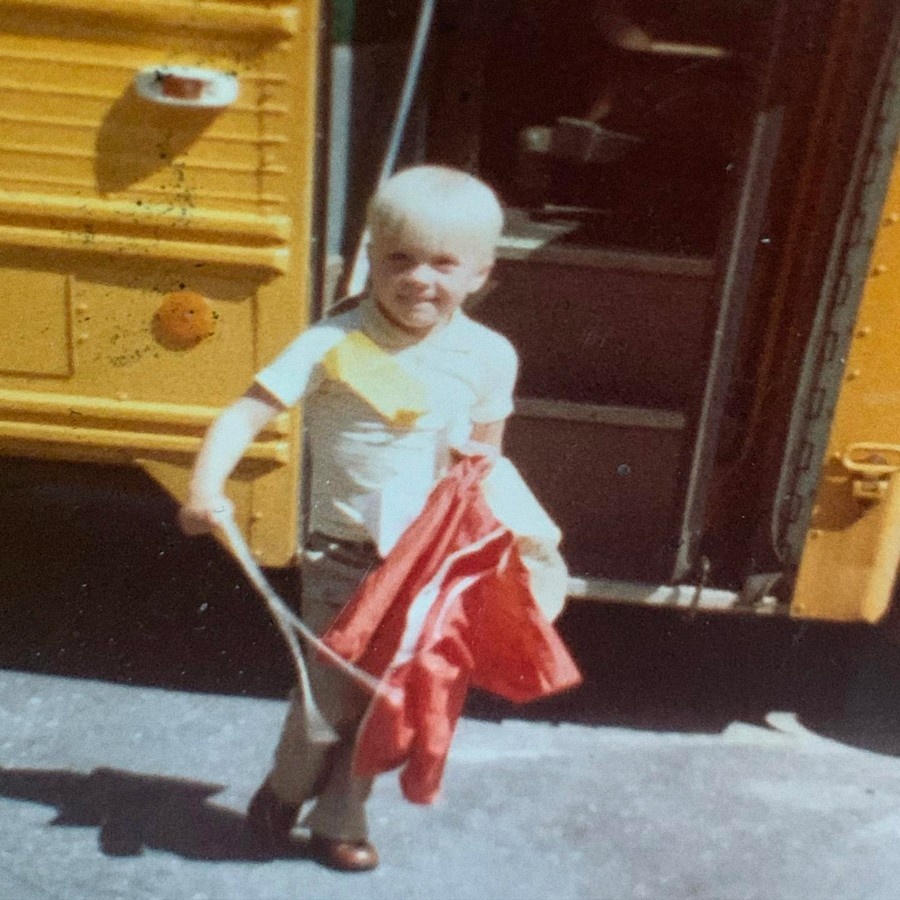 School-aged Traver Boehm in front of open school bus doors