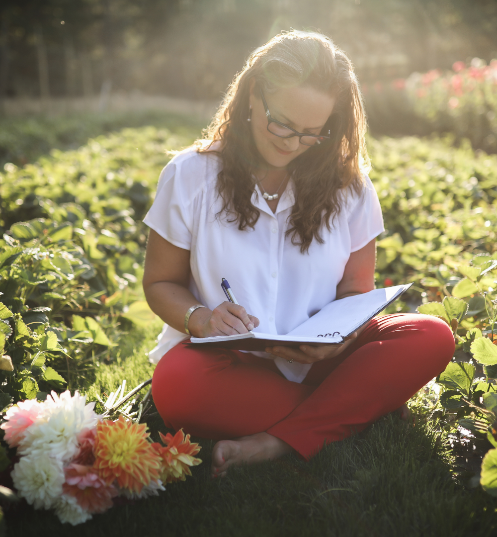 spa business coach sitting in a field with flowers, writing in a journal